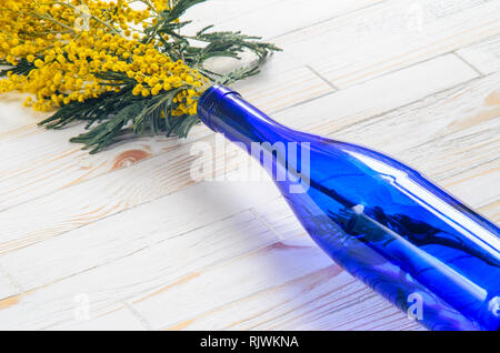 Mimosa Blumenstrauß in einer blauen Glasflasche auf weißem Holz Tisch Stockfoto