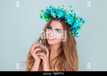 Schöne junge Frau lächelnd Modell mit Anemone blumen Kopf floral Kopfband Krone, Holding neues Parfüm Flasche mir in die Kamera lächeln, isolieren Stockfoto