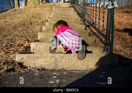 Ein Kleinkind Mädchen kriecht auf einen Flug der Steintreppe an einem sonnigen Tag. Stockfoto