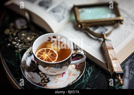 Cocktail in einer Tasse Tee und einem offenen Buch Stockfoto