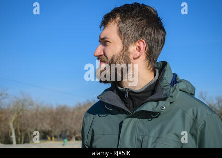 Porträt einer stattlichen nachdenklicher junger Mann mit Bart in die Ferne schaut. träumen Kerl auf dem Hintergrund des blauen Himmels und Feld. sonnigen Tag Stockfoto