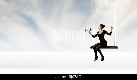 Frau mime im schwarzen Anzug sitzt auf Swing. Mixed Media Stockfoto