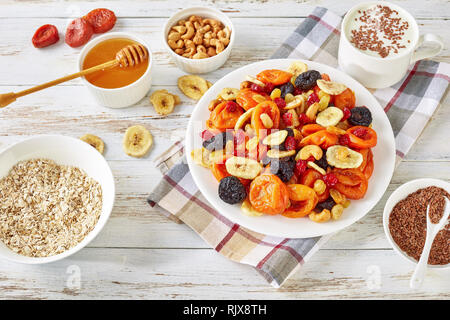 Getrocknete Früchte und Mutter Mix Schüssel - Bananenscheiben, Aprikosen, Rosinen, Pflaumen, Kirschen und Cashew auf einem rustikalen Tisch mit Porridge, Honig in eine Schüssel geben und Yog Stockfoto