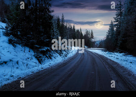 Straße durch Kiefernwald in Bergen in der Nacht im Vollmond Licht. geheimnisvolle Transport Winterlandschaft. Pfad Wicklung unten am Hügel Stockfoto