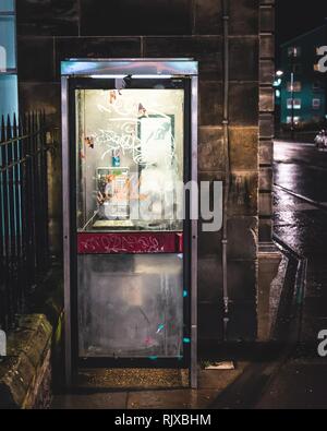 Eine alte, zerstörte Telefonzelle bis in die Nacht an der Ecke der Straße in Edinburgh, Schottland, beleuchtet Stockfoto