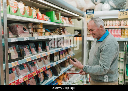 Älterer Mann da sein Essen Einkaufen im Supermarkt und ist auf seine Einkaufsliste auf seinem Smartphone. Stockfoto