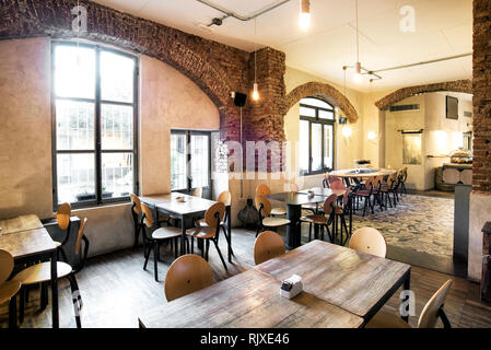 Tische und Stühle in einem leeren Restaurant im Landhausstil mit großen Bogenfenstern und viel Sonnenlicht Stockfoto