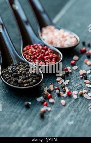 Studio shot von drei Löffel mit groben Salz Rosa, Schwarz und rosa Pfeffer auf dunklem Hintergrund Stockfoto