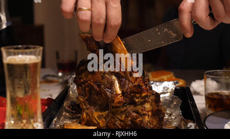 Männliche Hände, die Messer und schneiden Rindfleisch Rippe Braten auf Tisch Stockfoto