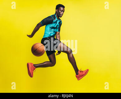 Junge Basketballspieler Dribbling eine Kugel über gelben Hintergrund. Mann in Sportswear üben Basketball. Stockfoto