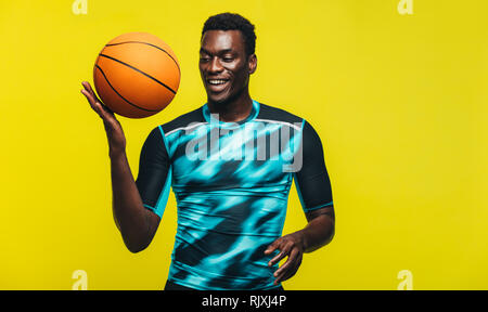 Afrikanischer mann mit einen Basketball in der Hand. Selbstbewussten Jungen Basketball Spieler gegen gelben Hintergrund. Stockfoto