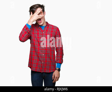 Junger stattlicher Mann mit Brille über isolierte Hintergrund peeking im Schock für Gesicht und Augen mit der Hand, schauen durch die Finger mit embarrasse Stockfoto