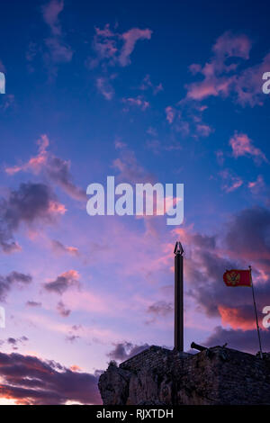 Statue Obelisk und montenegrinische Flagge im Wind flattern in der Festung an der Spitze der Klippen in Petrovac Küste bei Dämmerung, Montenegro Stockfoto