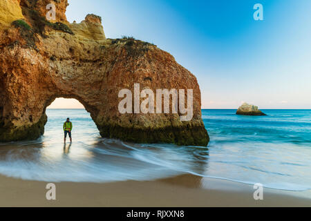 Mann stand unter Natural Arch von Cliff, Blick auf das Meer, Alvor, Algarve, Portugal, Europa Stockfoto