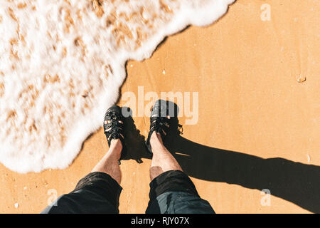 Hohe Betrachtungswinkel von Mans Füße paddeln durch Wasser am Strand, horizontal Stockfoto