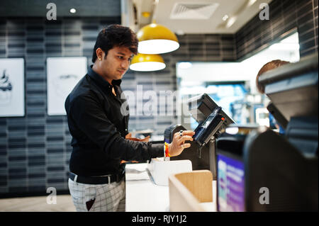 Indische Mann hält per Kreditkarte Bezahlen an der Kasse mit der Bildschirm und Payment Terminal in Essen Cafe. Stockfoto