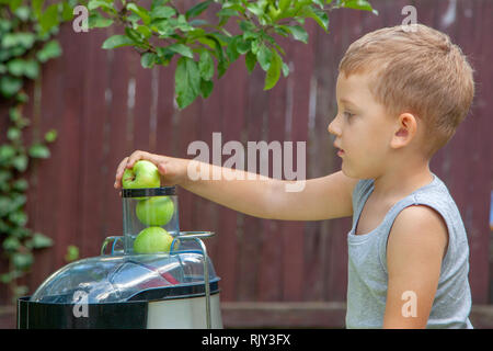 Junge Kind macht Saft aus grünen Äpfel im Entsafter im Freien Stockfoto
