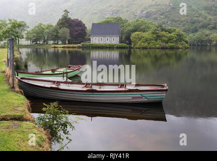 Die St. Finbarr Oratorium über den See bei Gougane Barra, County Cork, Republik Irland gesehen. Eire. Ruderboote im Vordergrund. Stockfoto