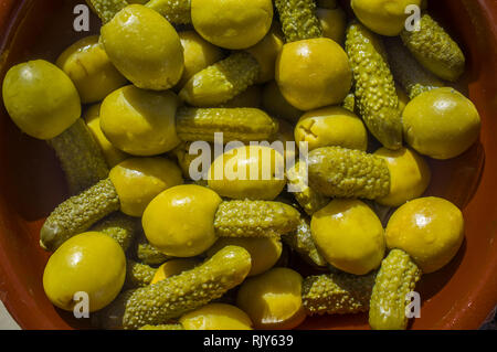 Eingelegte Oliven gefüllt mit Gurken auf Lehm Schüssel serviert. Overhead Schuß über glasierte Fliesen Mosaik Tisch Stockfoto