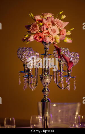 Tabelle Mittelstück, eine schöne Kristallleuchter stil Kerzenhalter mit vier Hohl - geschnitzt, die Schüsseln für Kerzenständer mit einem Blumenstrauß auf der Oberseite Stockfoto