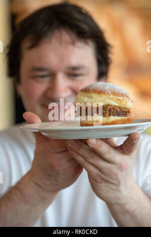 Miesbach, Deutschland. 07 Feb, 2019. Bäckermeister Florian Perkmann hält einen Donut mit Meat Loaf und süßen Senf gekrönt. Nach dem Leberkäs-Krapfen aus Oberbayern, die Goaßmaß-Krapfen kommt jetzt aus Niederbayern. Eine Goass Maßnahme ist ein gemischtes Getränk Bier, Cola und kirschlikör. (Dpa vom 09.02.2019) Credit: Lino Mirgeler/dpa/Alamy leben Nachrichten Stockfoto