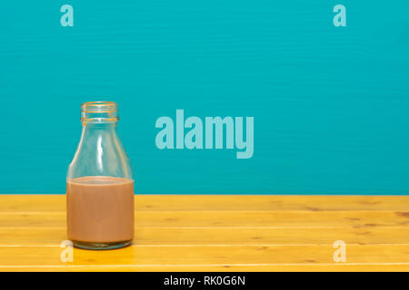 Ein Drittel pint Glas Milch Flasche halb voll mit Schokolade Milchshake, auf einen hölzernen Tisch gegen einen hellen Teal gemalten Hintergrund Stockfoto