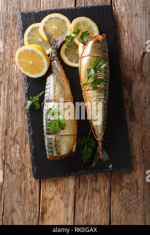 Ganz frisch geräucherte Makrele mit Zitronen und Petersilie closeup auf einem schwarzen Schiefer Brett am Tisch serviert. Vertikal oben Ansicht von oben Stockfoto