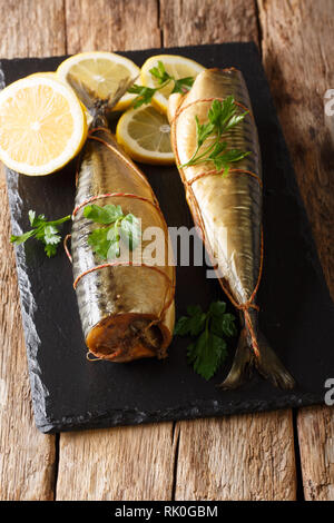 Geräucherte Makrele Essen serviert mit Zitronen und Petersilie closeup auf einen schwarzen Stein Brett auf den Tisch. Vertikale Stockfoto