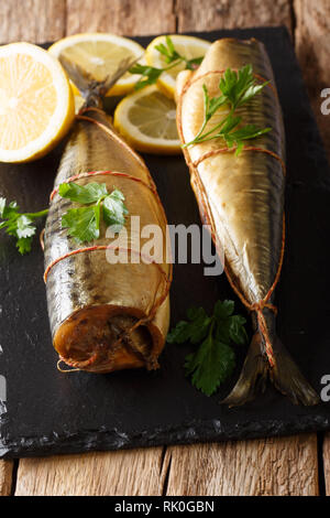 Ganz frisch geräucherte Makrele mit Zitronen und Petersilie closeup auf einem schwarzen Schiefer Brett auf den Tisch serviert. Vertikale Stockfoto