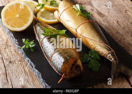 Köstliche ganze geräucherte Makrele mit Zitronen und Petersilie closeup auf einem schwarzen Schiefer Board auf dem Tisch. Horizontale Stockfoto