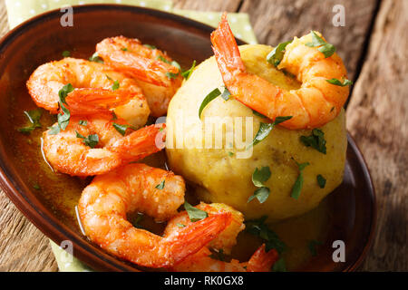 Würzige mofongo mit Kochbananen, Knoblauch und chicharron mit Garnelen und Brühe close-up auf einem Schild auf dem Tisch serviert. Horizontale Stockfoto