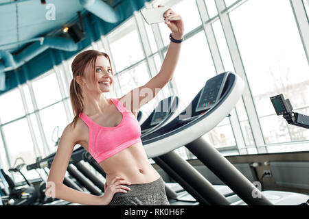 Junge Frau im Gym gesunde Lebensweise ständigen Holding Smartphone unter selfie Fotos suchen Kamera lächelt fröhlich Posieren Stockfoto