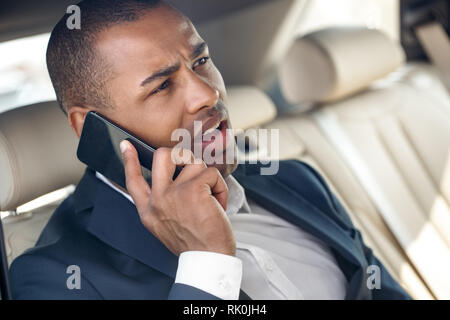 Junge afrikanische amerikanische Geschäftsmann im Auto sitzen Reden auf dem Smartphone Diskussion Projekt mit Business Partner ernst close-up Stockfoto