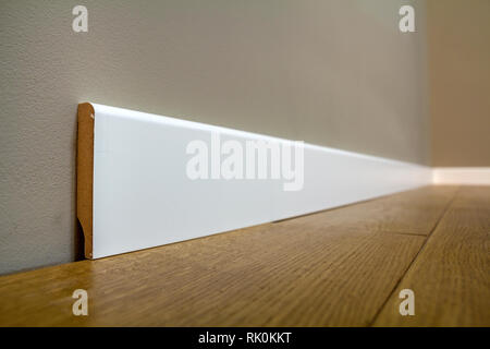 Holz- oder Kunststoff Weiß, Sockel Installation in großen leeren Raum auf Holzboden und weiß verputzt verputzten Wänden Hintergrund. Details im Innenraum. Stockfoto