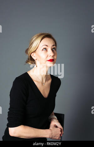 Porträt der schönen Frau in einem schwarzen Kleid vor grauem Hintergrund Stockfoto