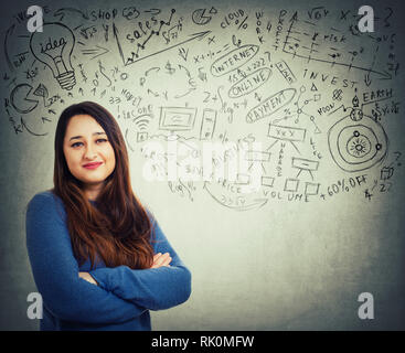 Selbstbewussten jungen Frau Hände gekreuzt über graue Wand Hintergrund mit viel Ideen und Projekte Skizzen isoliert. Entscheidungsfindung in Unternehmen Konzept. Stockfoto