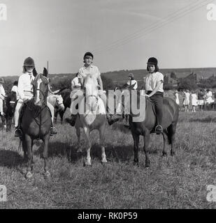 1964, Mädchen auf Ponys oder kleine Pferde in ein Feld in einem reiten Gymkhana, England, UK, ein Reitzentrum, auch mit unterschiedlichen Reiterinnen und Rassen. Stockfoto