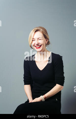 Porträt der schönen Frau in einem schwarzen Kleid vor grauem Hintergrund Stockfoto