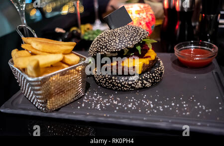 Lecker schwarz Burger, Pommes frites in Korb und Ketchup auf dem Schwarzen Brett serviert. Copy-Flag in Bun für Ihren individuellen Text. Stockfoto