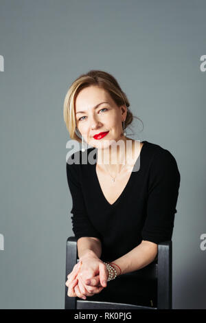 Porträt der schönen Frau in einem schwarzen Kleid vor grauem Hintergrund Stockfoto