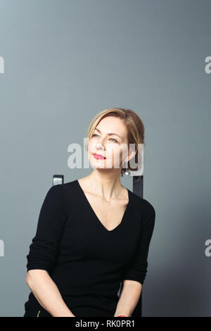 Porträt der schönen Frau in einem schwarzen Kleid vor grauem Hintergrund Stockfoto