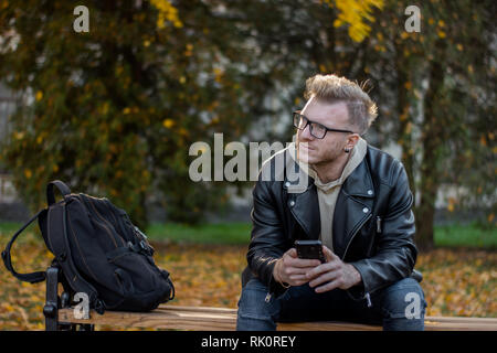 Träumen lächelnden Kerl mit einem Telefon in legere Kleidung, auf der Bank sitzen Stockfoto
