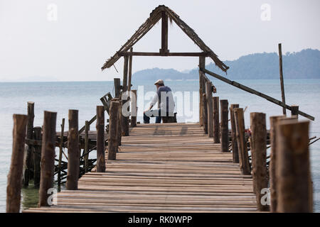 Trauriger alter Mann in einem Gap sitzen auf dem Pier und den Blick auf das Meer Stockfoto