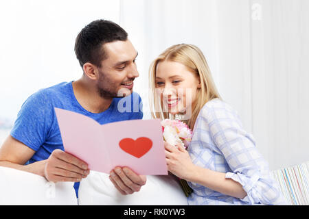 Glückliches Paar mit Grußkarte und Blumen Stockfoto