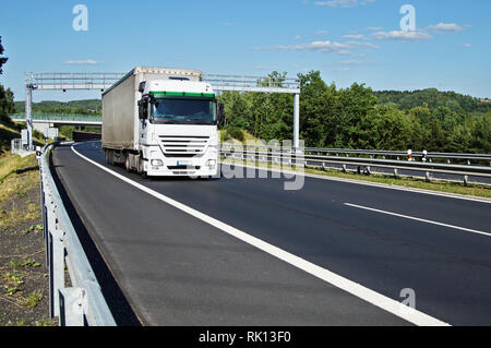 Weisse Truck durch die elektronische Mautstellen auf dem Asphalt Autobahn in einem bewaldeten Landschaft. Brücke und bewaldete Berge im Hintergrund. W Stockfoto