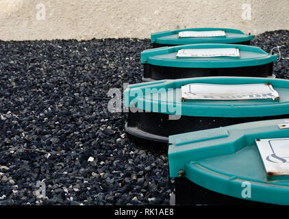 Vier große zylindrische Behälter, mit grünem Deckel bedeckt, meist unterirdisch mit kleinen schwarzen Steinen auf dem Boden platziert. Stockfoto