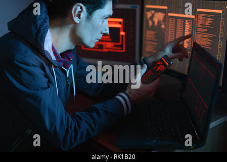 Die männlichen Hacker in der Haube weist seinen Finger auf dem Display die Anzeige der Position der Abwehr von Cyberattacken und Hacking Daten auf dem Bildschirm Hintergrund Stockfoto