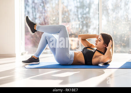 Junge passende Frau trainieren im Fitnessraum liegen auf der Matte, Bein heben und verdrehen Übungen. Junge attraktive Frau, abs-Training. Fitness Frau tun Stockfoto