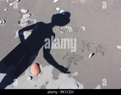 Der Schatten einer Person auf einem Black Sand Beach anzeigen Das Mandarin Zeichen für die Worte, die Familie und die Liebe Stockfoto