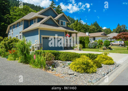 Fragment einer Familie Haus mit Garten- und Landschaftsbau an der Vorder- und Hintergrund des blauen Himmels. Haus mit grosse Garage Tor Stockfoto